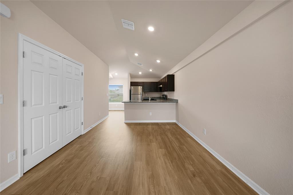 An open-concept living area features wood-look flooring, a white double-door closet, and a kitchen — 11057 & 11059 PENDLETON AVENUE, ENGLEWOOD, FL