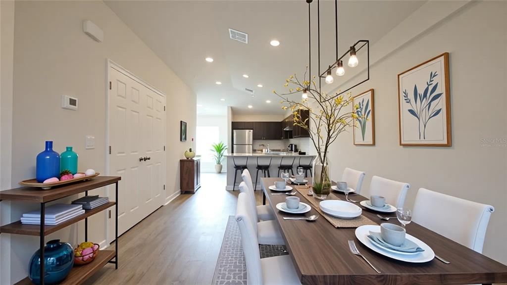 A dining area with a wooden table, chairs, and a kitchen visible in the background — 11057 & 11059 PENDLETON AVENUE, ENGLEWOOD, FL