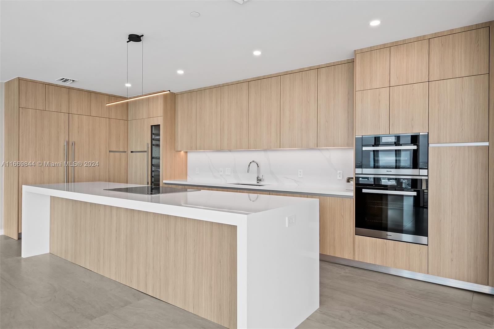 A modern kitchen features light wood cabinetry, a white waterfall island, and stainless steel appliances — 851 NE 1st Ave # 5412, Miami FL 33132, MIAMI, FL