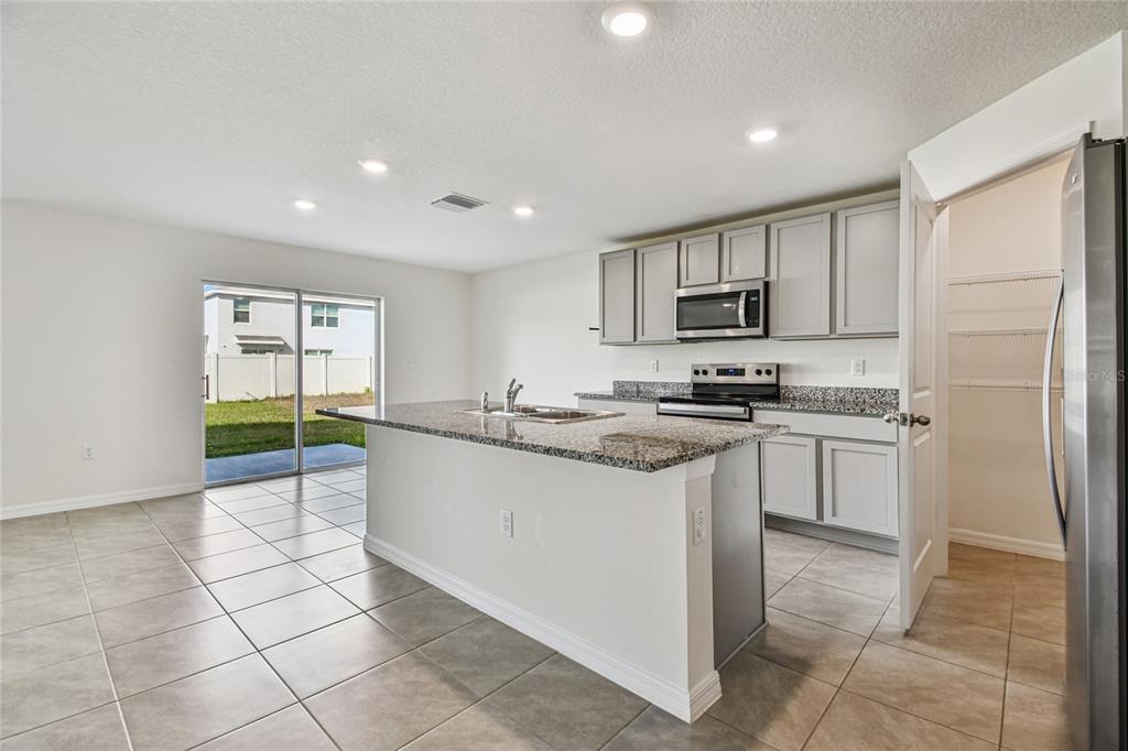 A kitchen with a granite island, gray cabinets, stainless steel appliances, and tile flooring — 9208 MISSION BAY PLACE, TAMPA, FL