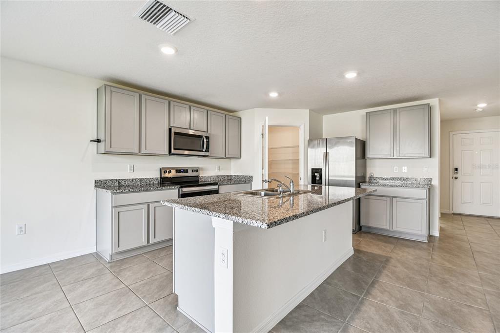 A kitchen features gray cabinets, granite countertops, a center island, and stainless steel appliances — 9208 MISSION BAY PLACE, TAMPA, FL