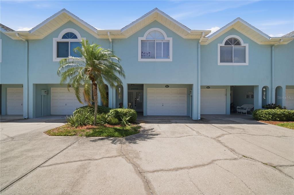 A row of light blue townhomes features three garage doors and a small palm tree — 643 GARLAND CIRCLE, INDIAN ROCKS BEACH, FL