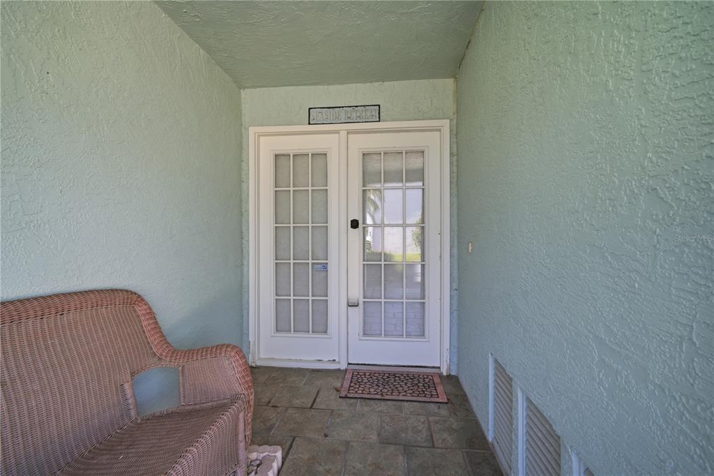 A covered patio features a wicker loveseat, tiled flooring, and a double glass-paned entry door — 643 GARLAND CIRCLE, INDIAN ROCKS BEACH, FL