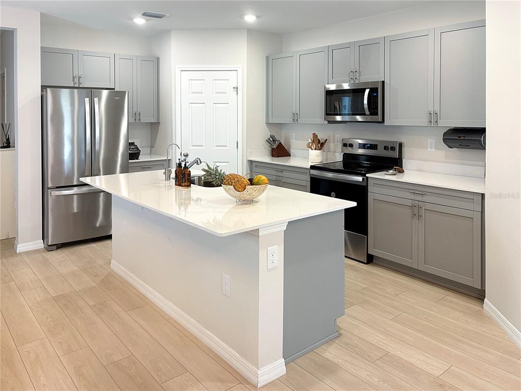 A kitchen features gray cabinets, stainless steel appliances, a white island, and light wood flooring — 3798 KING HILL DRIVE, HAINES CITY, FL
