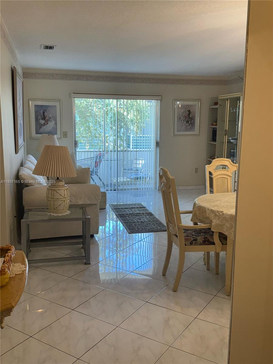 A living and dining area features light-colored tile floors, a glass-topped table, and sliding glass doors — 1395 NE 167th St # 203, Miami FL 33162, MIAMI, FL
