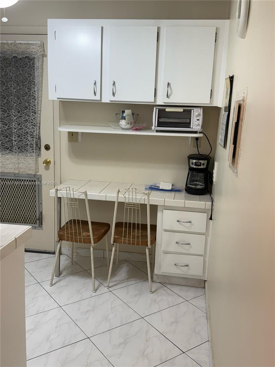 A kitchen area features white cabinets, a tiled counter with two chairs, and a coffee maker — 1395 NE 167th St # 203, Miami FL 33162, MIAMI, FL