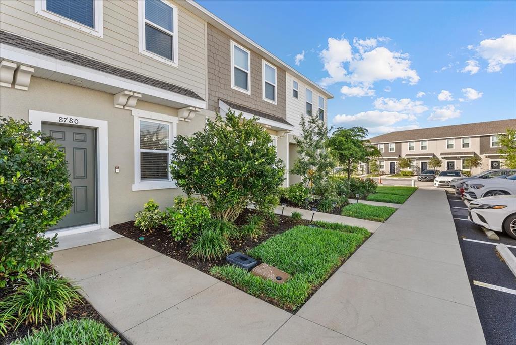 A two-story townhouse exterior features a gray front door, tan siding, and a concrete walkway — 8780 DAYBREAK STREET, SARASOTA, FL