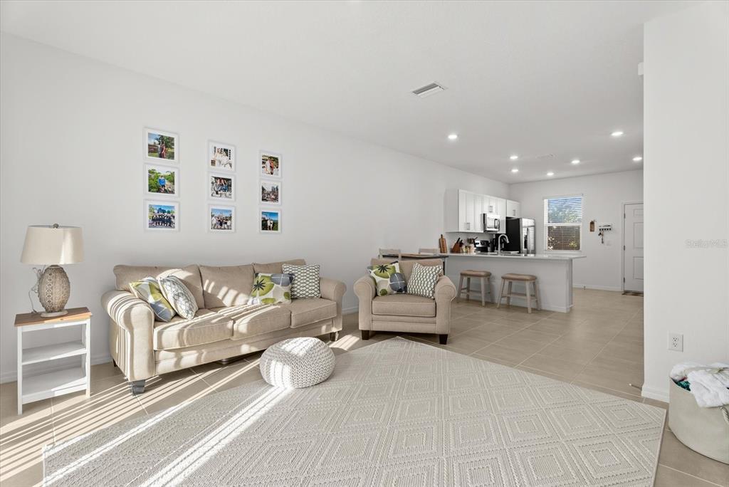 A living room with a beige sofa, armchair, area rug, and an open kitchen beyond — 8780 DAYBREAK STREET, SARASOTA, FL