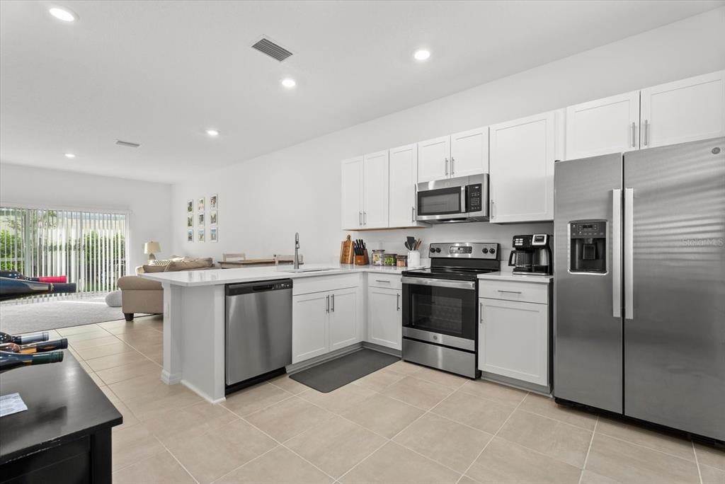 A modern kitchen features white cabinets, stainless steel appliances, and a breakfast bar island — 8780 DAYBREAK STREET, SARASOTA, FL
