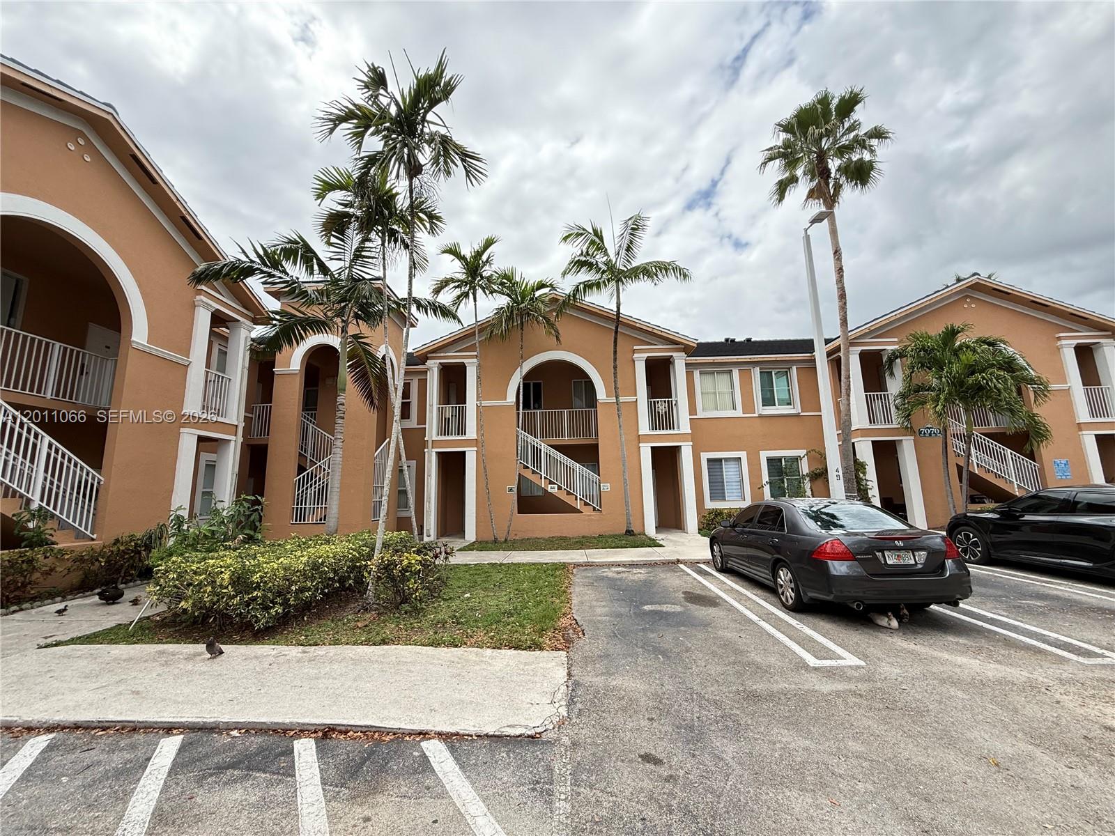 An exterior view of a multi-story apartment building with palm trees and a parking lot — 7070 NW 177th St # 10, Hialeah FL 33015, HIALEAH, FL