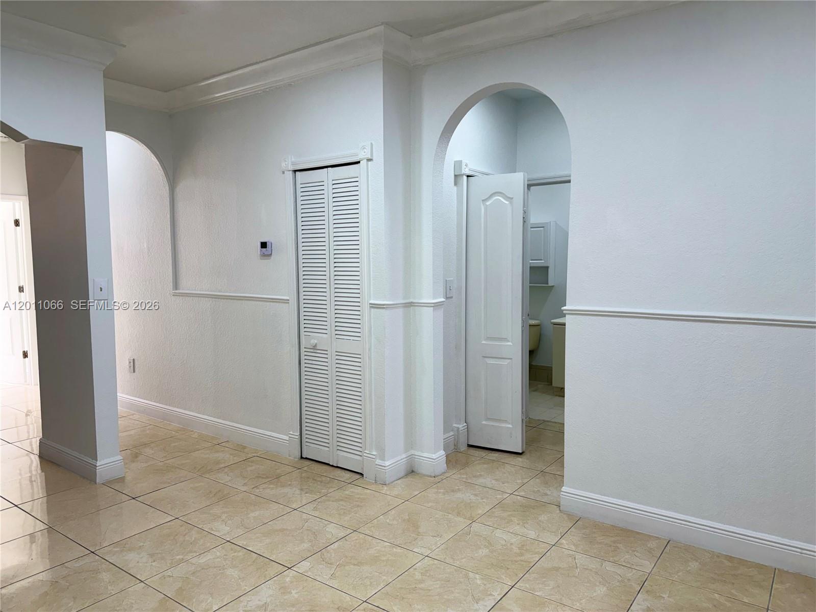 A hallway with tiled floors, arched doorways, and a closet with louvered doors — 7070 NW 177th St # 10, Hialeah FL 33015, HIALEAH, FL