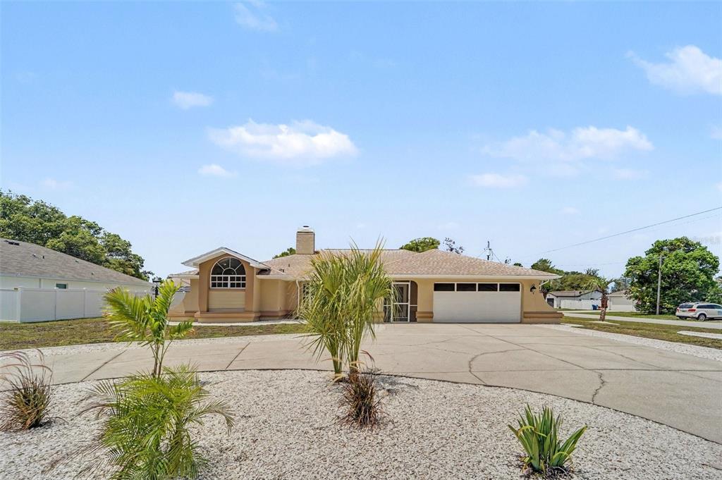 A single-story house with a beige stucco exterior, a two-car garage, and a gravel yard — 8500 BAY DRIVE, SPRING HILL, FL
