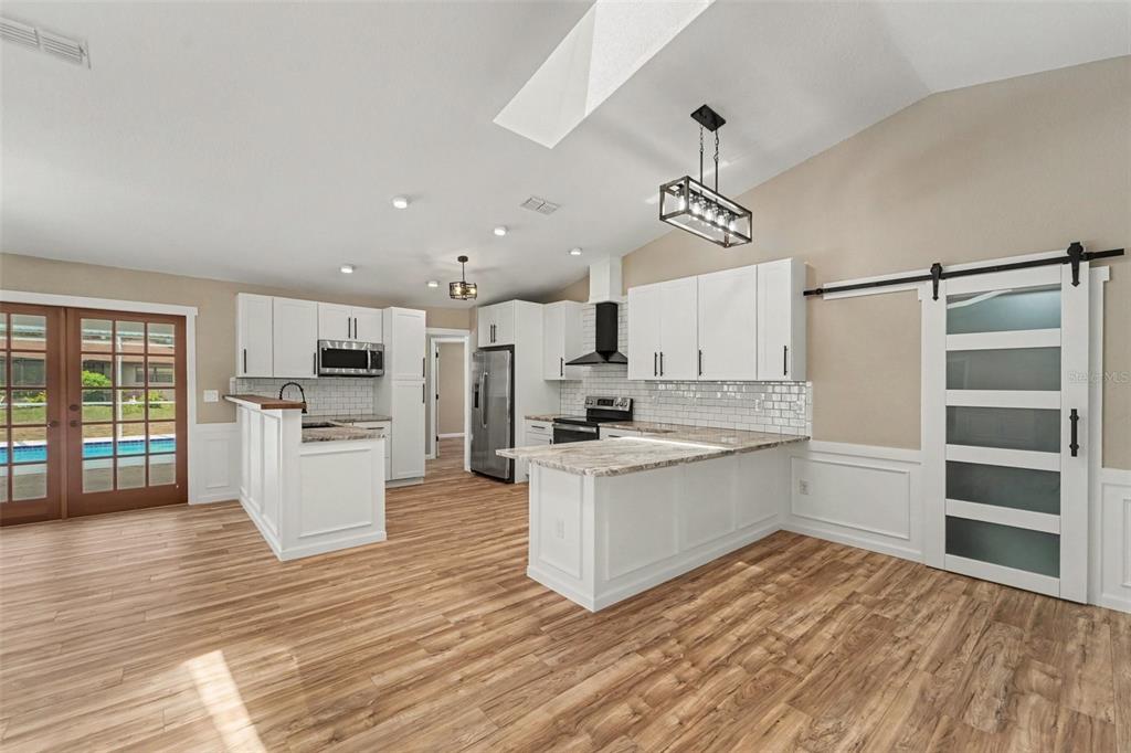 A kitchen with white cabinets, granite countertops, wood-look flooring, and a sliding barn door — 8500 BAY DRIVE, SPRING HILL, FL