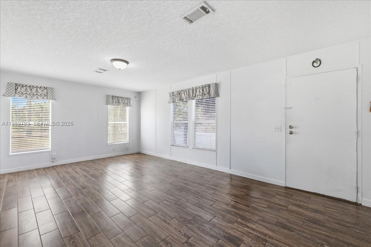 An empty room features white walls, wood-look flooring, three windows with valances, and a door — 415 S Kennel St, Clewiston FL 33440, CLEWISTON, FL