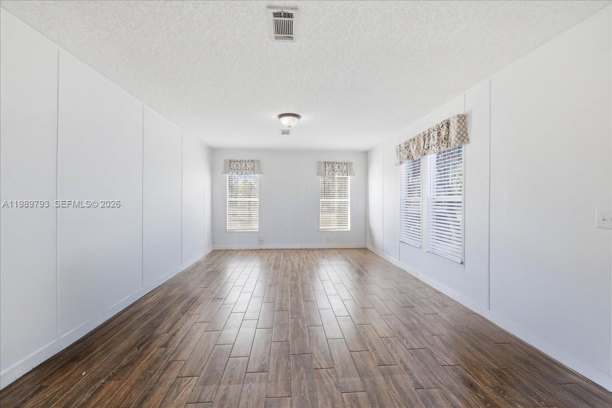 An empty room features white walls, wood-look flooring, and several windows with blinds — 415 S Kennel St, Clewiston FL 33440, CLEWISTON, FL