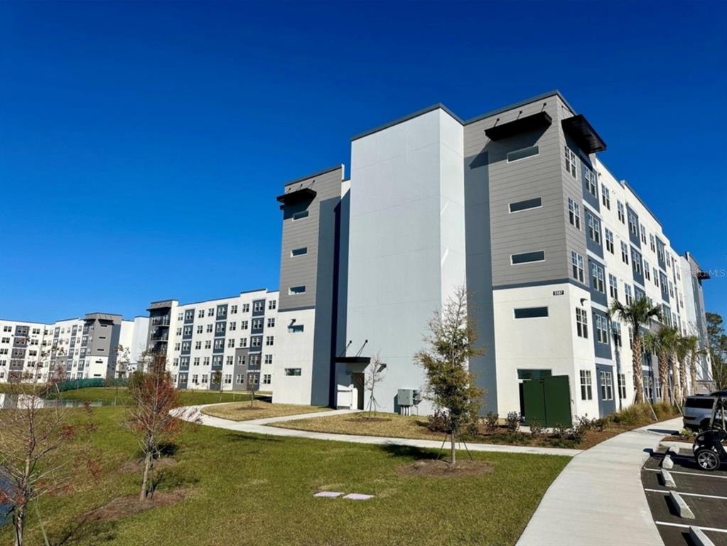 A modern multi-story apartment building with gray and white siding stands next to a sidewalk — 5587 MILLENIA BOULEVARD UNIT 213, ORLANDO, FL