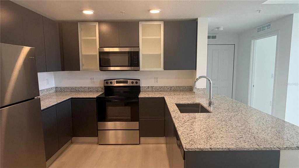 A modern kitchen features dark cabinetry, stainless steel appliances, and speckled granite countertops — 5587 MILLENIA BOULEVARD UNIT 213, ORLANDO, FL