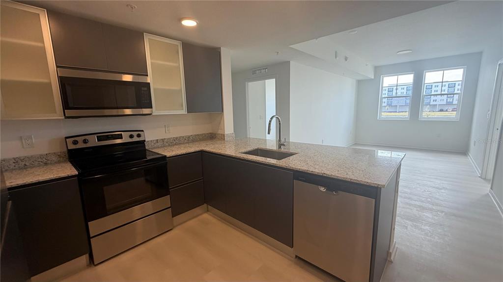 A modern kitchen features dark gray cabinetry, stainless steel appliances, and light granite countertops — 5587 MILLENIA BOULEVARD UNIT 213, ORLANDO, FL