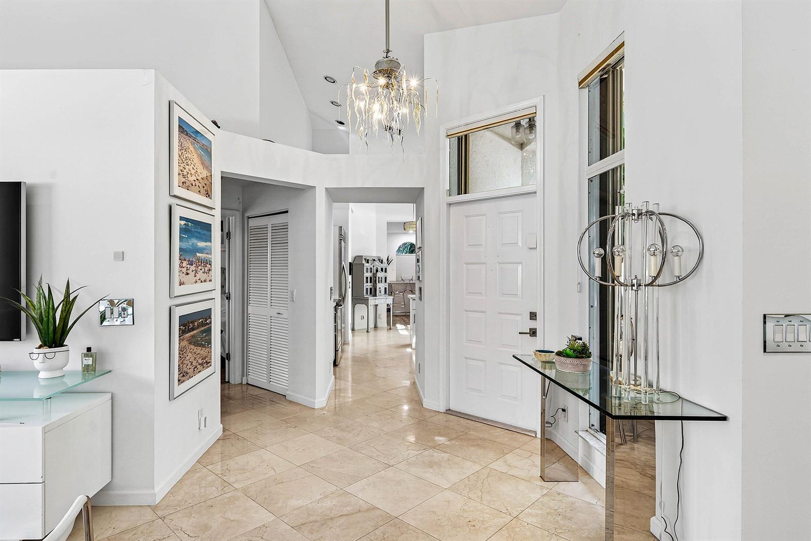 A bright entryway features a glass console table, a chandelier, and light-colored tile flooring — 6601 NW 26th Way, Boca Raton FL 33496, BOCA RATON, FL