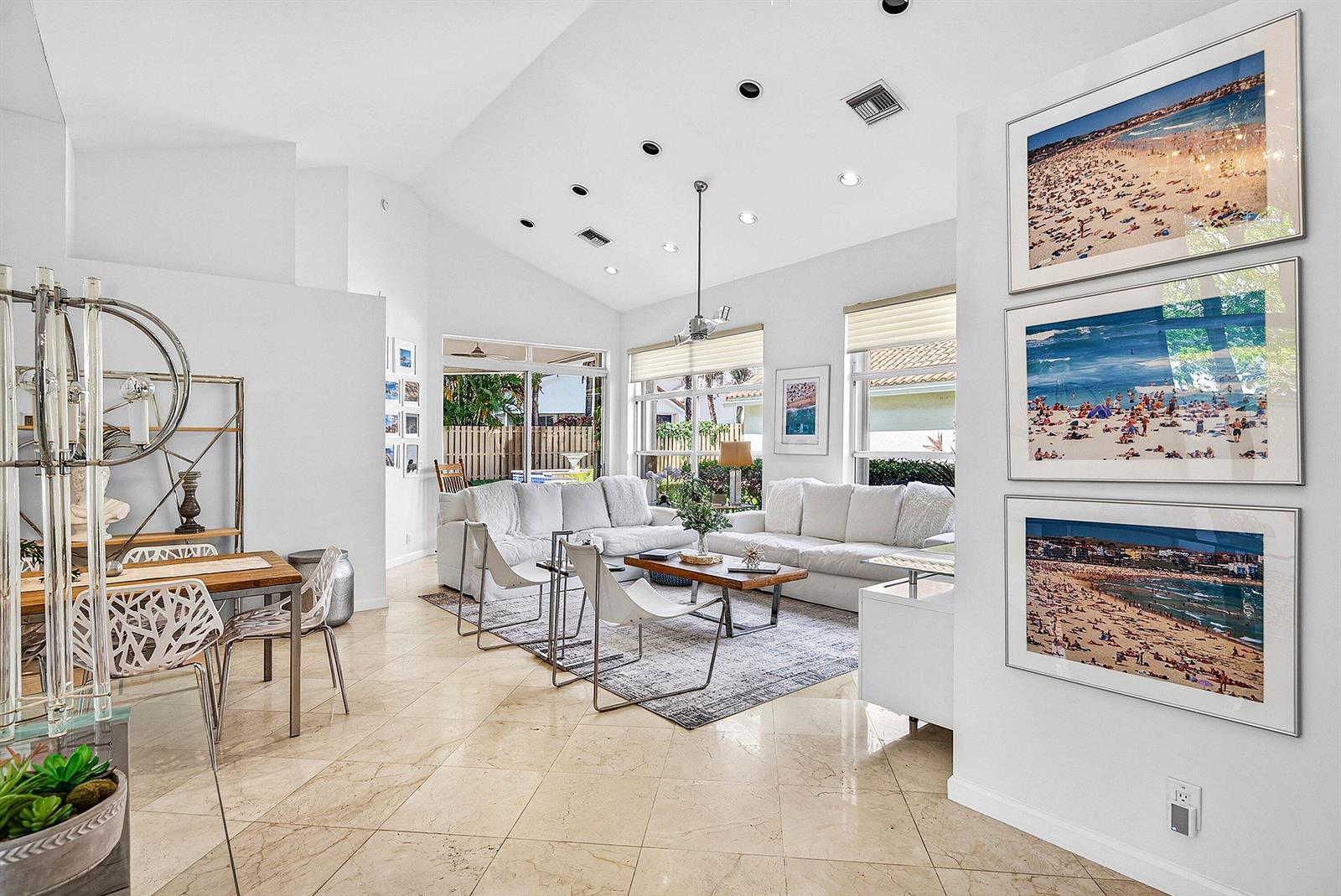 A bright living room features vaulted ceilings, white sofas, tiled floors, and three beach photographs — 6601 NW 26th Way, Boca Raton FL 33496, BOCA RATON, FL