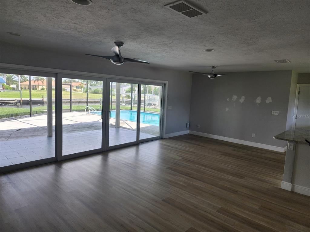 A living room with wood-look flooring, ceiling fans, and sliding glass doors overlooking a pool — 5325 COCOA COURT, CAPE CORAL, FL