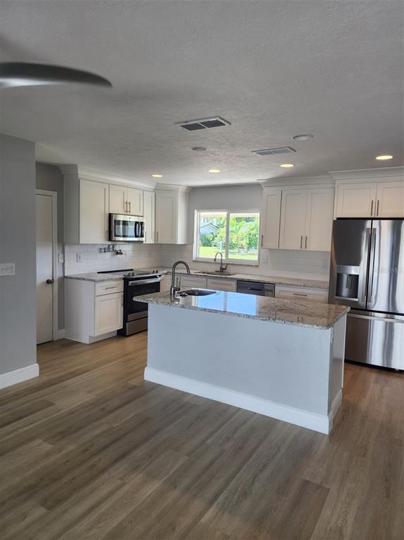 A kitchen features white cabinets, granite countertops, stainless steel appliances, and light wood-look flooring — 5325 COCOA COURT, CAPE CORAL, FL