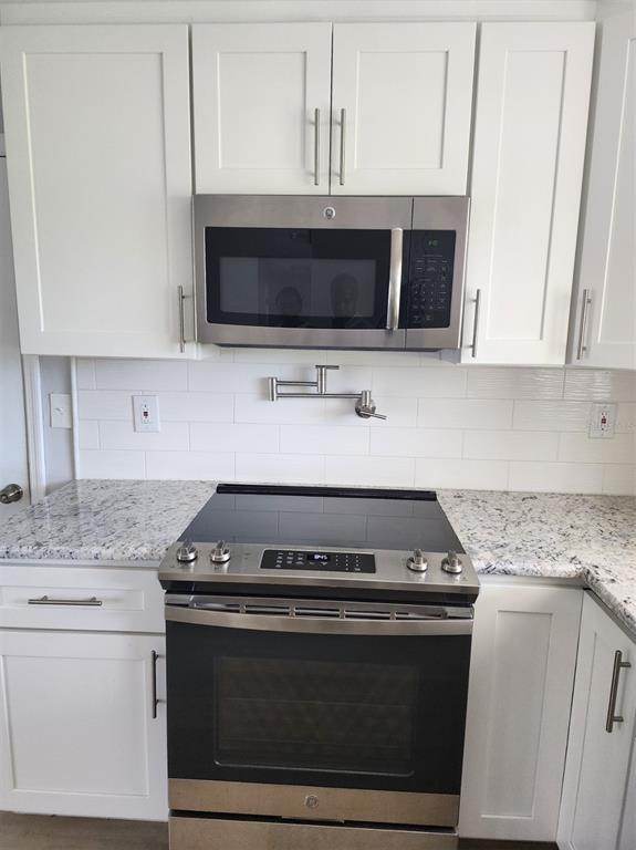 A kitchen features white cabinets, granite countertops, a stainless steel stove, and a wall-mounted pot filler — 5325 COCOA COURT, CAPE CORAL, FL
