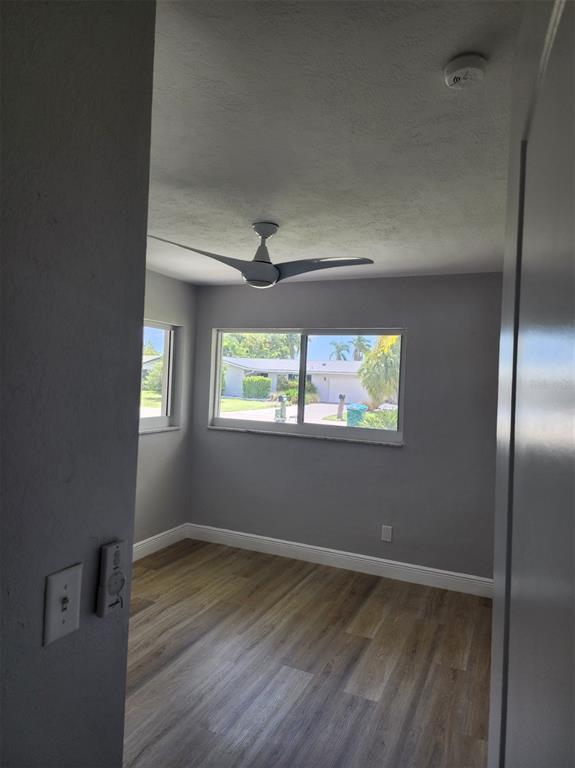 A bedroom with gray walls, wood-look flooring, a ceiling fan, and windows overlooking a neighborhood — 5325 COCOA COURT, CAPE CORAL, FL