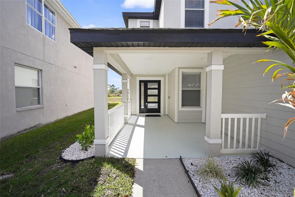 A covered front porch features a black-framed glass door, white railings, and light-colored siding — 20054 NOB OAK AVENUE, TAMPA, FL