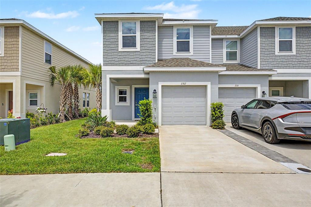 A two-story gray townhouse with a one-car garage and a small front lawn — 2307 PARAVANE WAY, WESLEY CHAPEL, FL