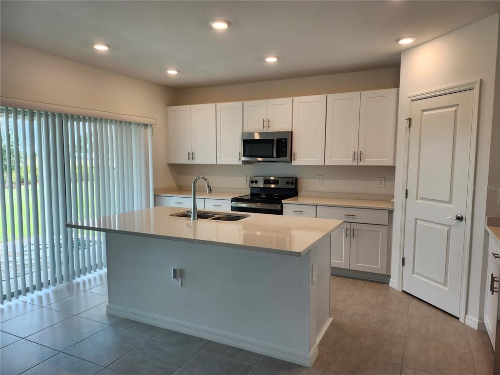 A kitchen with white cabinets, a central island, stainless steel appliances, and tile flooring — 1009 CALICO POINTE CIRCLE, GROVELAND, FL