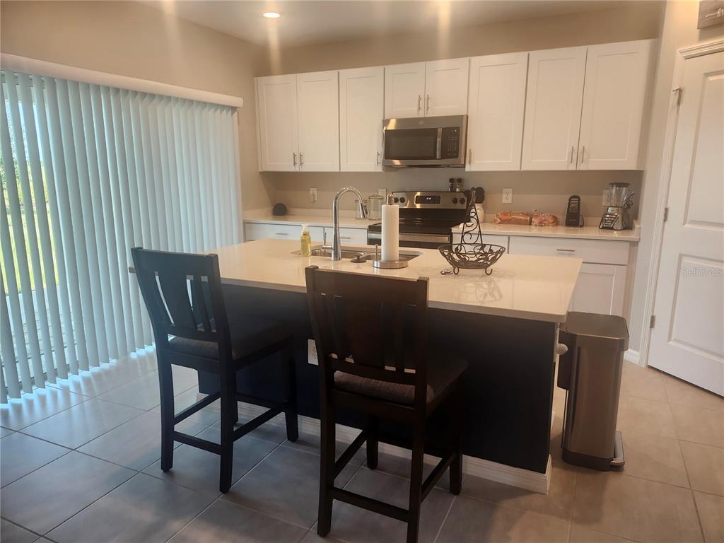 A kitchen features white cabinets, a central island with bar stools, and tiled flooring — 1009 CALICO POINTE CIRCLE, GROVELAND, FL
