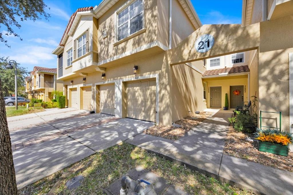 A multi-story tan townhouse exterior features multiple garage doors and a shared covered entryway — 7509 PELLHAM WAY UNIT 0, KISSIMMEE, FL
