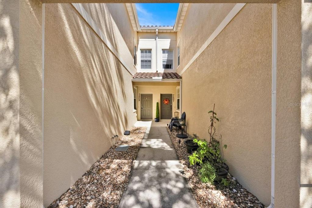 A narrow concrete walkway leads to two adjacent front doors between two tan stucco walls — 7509 PELLHAM WAY UNIT 0, KISSIMMEE, FL