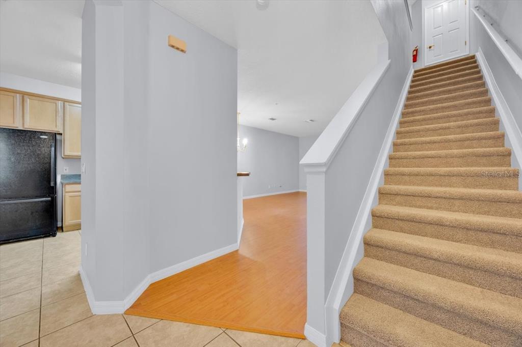 A carpeted staircase leads upstairs next to a kitchen and an open living area — 7509 PELLHAM WAY UNIT 0, KISSIMMEE, FL