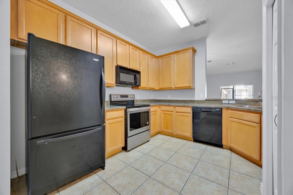 A kitchen features light wood cabinets, black appliances, and light-colored tile flooring — 7509 PELLHAM WAY UNIT 0, KISSIMMEE, FL