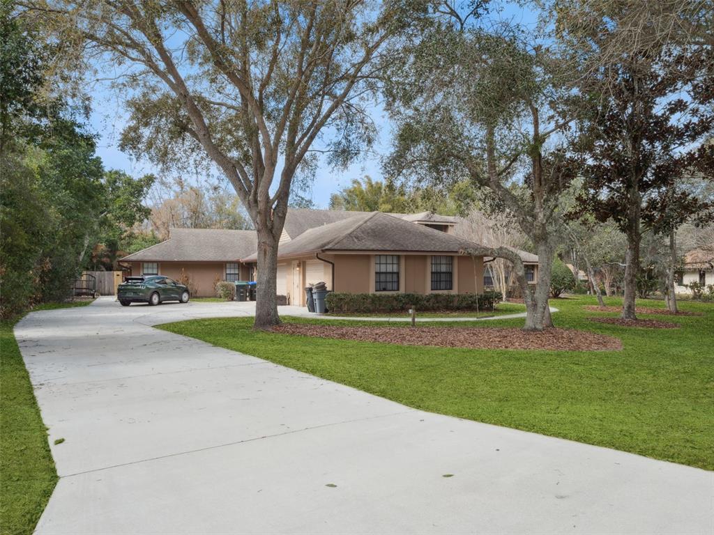 A tan single-story house with a large concrete driveway and mature trees in the yard — 5314 SHADYWOOD LANE, ORLANDO, FL