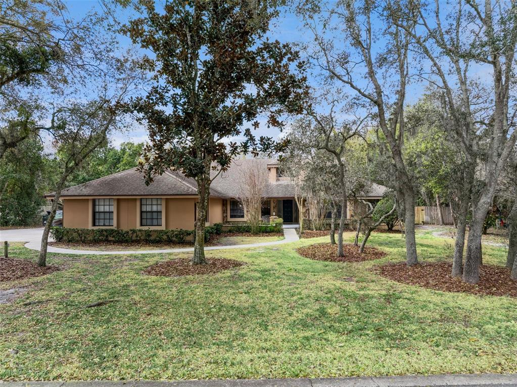 A single-story tan house with a dark roof sits behind trees on a grassy lot — 5314 SHADYWOOD LANE, ORLANDO, FL