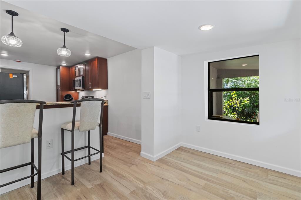 A kitchen with a breakfast bar and stools opens into a dining area with a window — 23094 CENTRAL AVENUE, PORT CHARLOTTE, FL