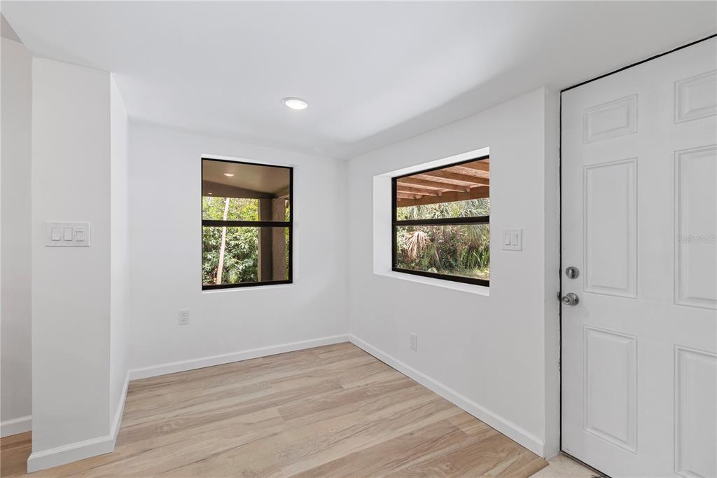 A bright, empty room features white walls, light wood-look flooring, and two windows — 23094 CENTRAL AVENUE, PORT CHARLOTTE, FL