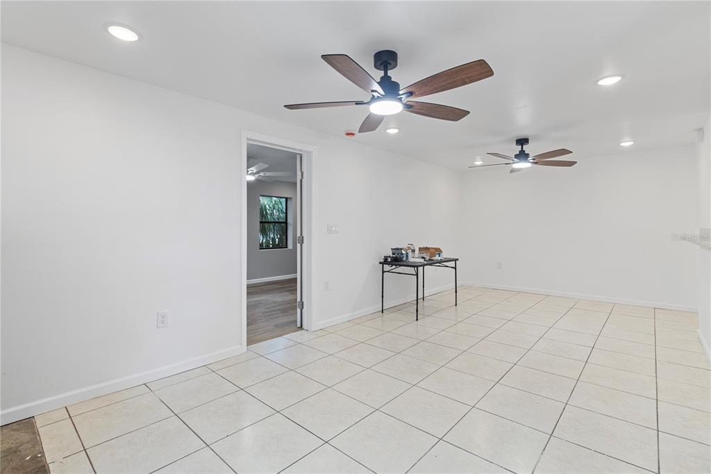 A bright, empty room features white walls, tiled flooring, two ceiling fans, and recessed lighting — 23094 CENTRAL AVENUE, PORT CHARLOTTE, FL