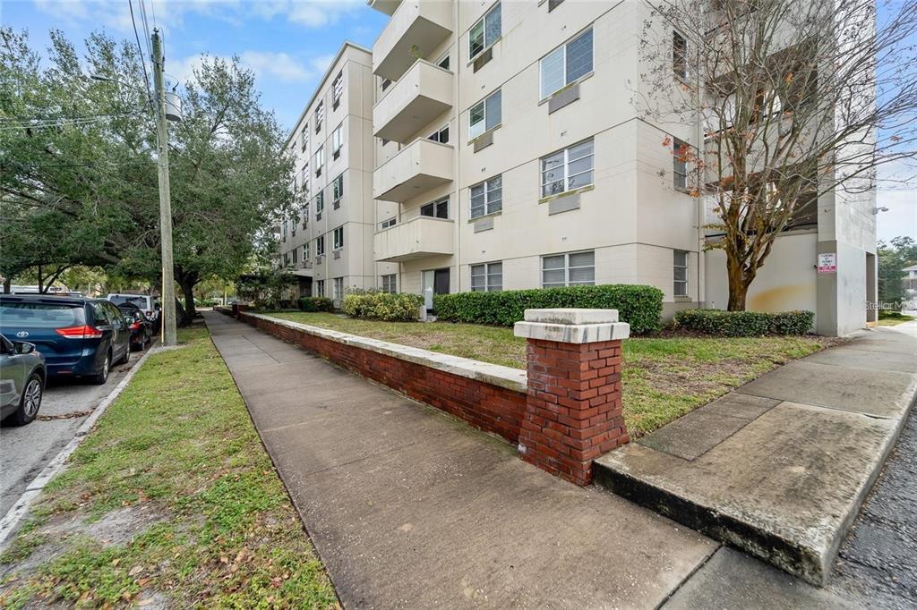 A multi-story apartment building with balconies stands behind a low brick wall and sidewalk — 406 S CEDAR AVENUE UNIT 307, TAMPA, FL