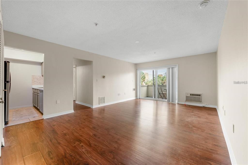 An empty living room features wood-look flooring, a sliding glass door, and an adjacent kitchen — 406 S CEDAR AVENUE UNIT 307, TAMPA, FL