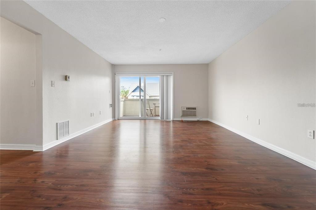 An empty living room features dark wood-look flooring, beige walls, and a sliding glass door — 406 S CEDAR AVENUE UNIT 307, TAMPA, FL