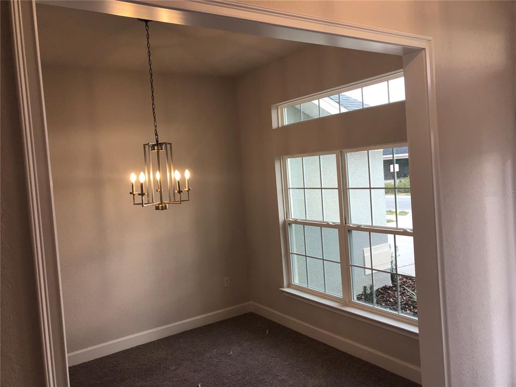 A small dining room features a modern chandelier, carpeted flooring, and large windows — 8744 SE 162ND STREET, SUMMERFIELD, FL