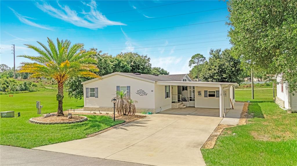 A single-story manufactured home features a concrete driveway, a carport, and a palm tree — 58 FLORENCE BOULEVARD, DEBARY, FL