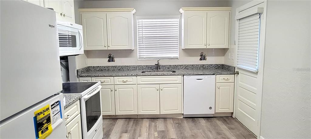 A kitchen features white cabinets, granite countertops, stainless steel appliances, and wood-look flooring — 340 TROPICAL LN, ORMOND BEACH, FL