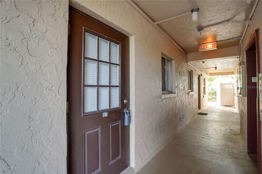 A brown door labeled 107 opens into a hallway with an elevator sign overhead — 4013 LAKE BAYSHORE DR UNIT 107, BRADENTON, FL