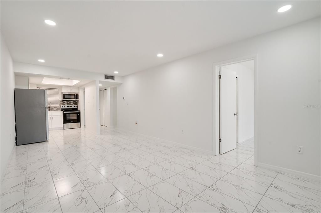 A bright, open-concept room features white marble-patterned tile flooring and a small kitchen area — 4013 LAKE BAYSHORE DR UNIT 107, BRADENTON, FL