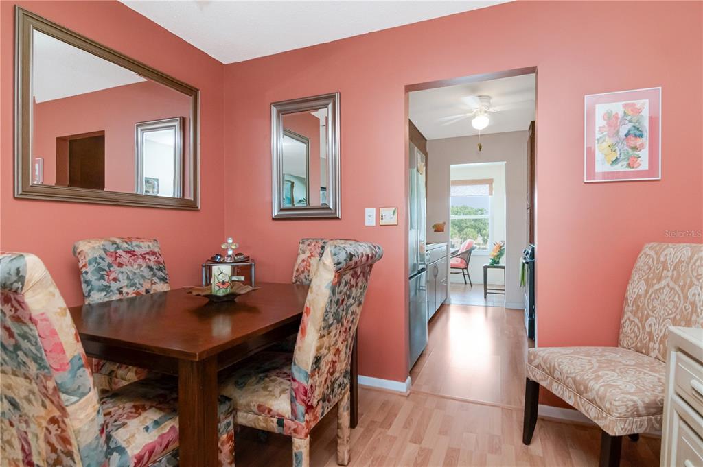 A dining room with coral walls, a wooden table, floral chairs, and two wall mirrors — 5935 30TH AVENUE S UNIT 206, GULFPORT, FL